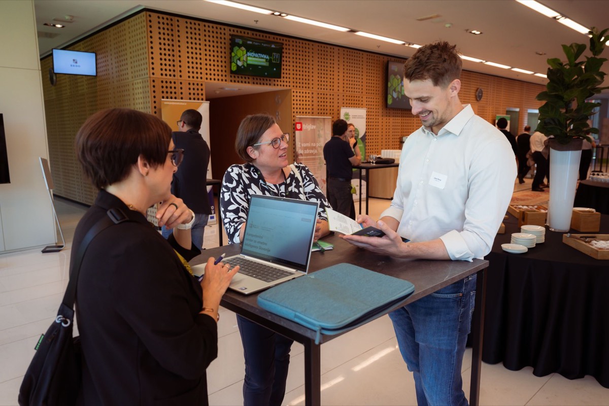 Jakob at a standing table with two visitors and a laptop at Dan inovativnosti, Brdo pri Kranju.