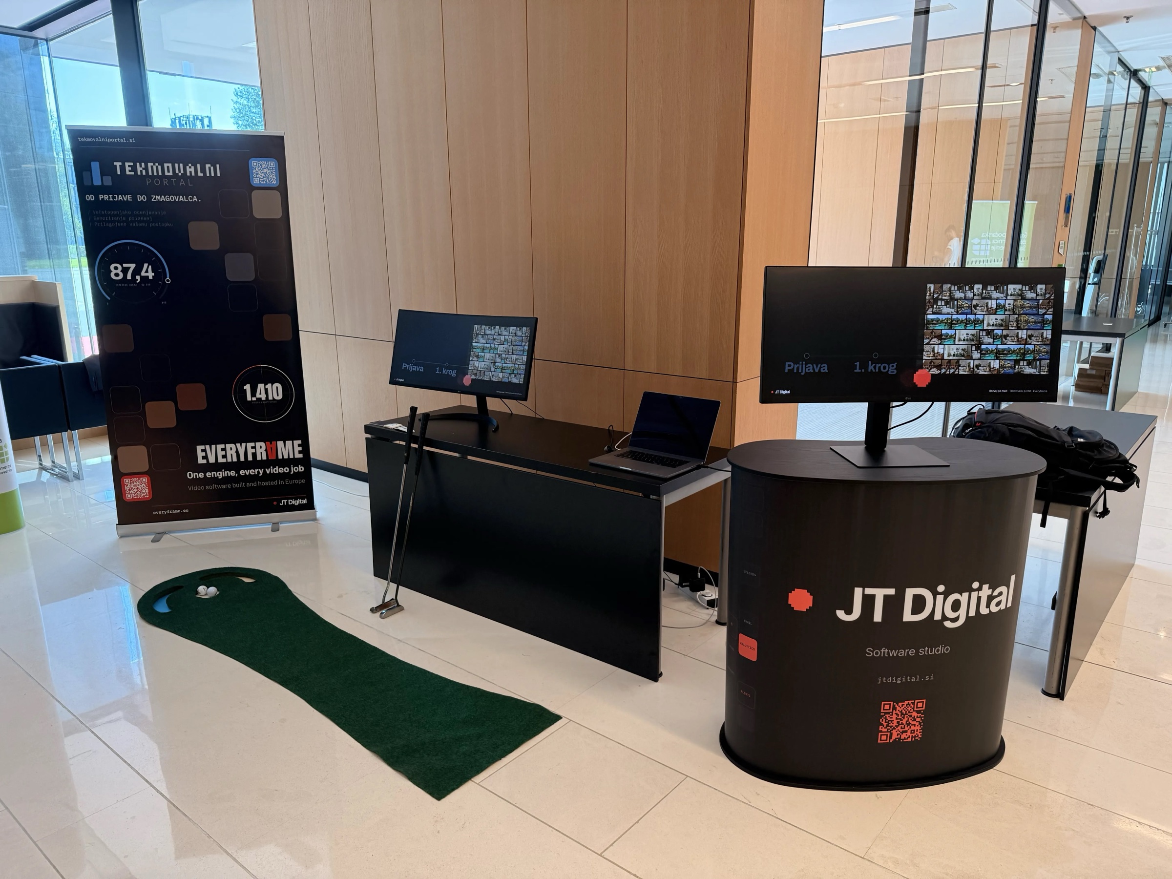The JT Digital stand at Dan inovativnosti 2026: the JT Digital counter, two screens showing GZS Inovacije entries, a laptop and a mini golf green